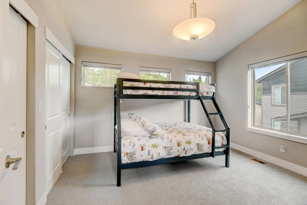 A cheerful bunk room with sturdy bunk beds positioned near windows, creating a bright and playful space for kids or adults. Soft lighting and thoughtful decor make it inviting for late-night stories and sleepovers.