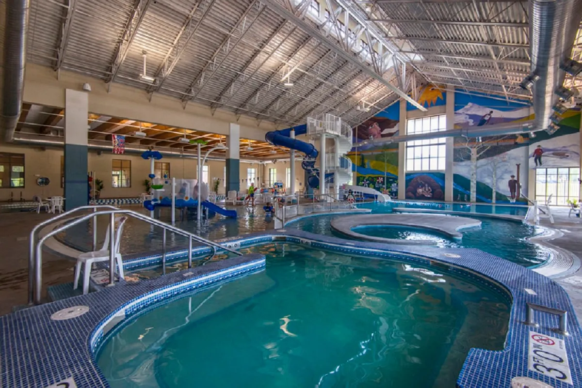 A vibrant indoor recreation center scene featuring children gleefully splashing in a pool, sliding down colorful water slides, and families gathered poolside. The space radiates energy and fun, emphasizing kid-friendly amenities.