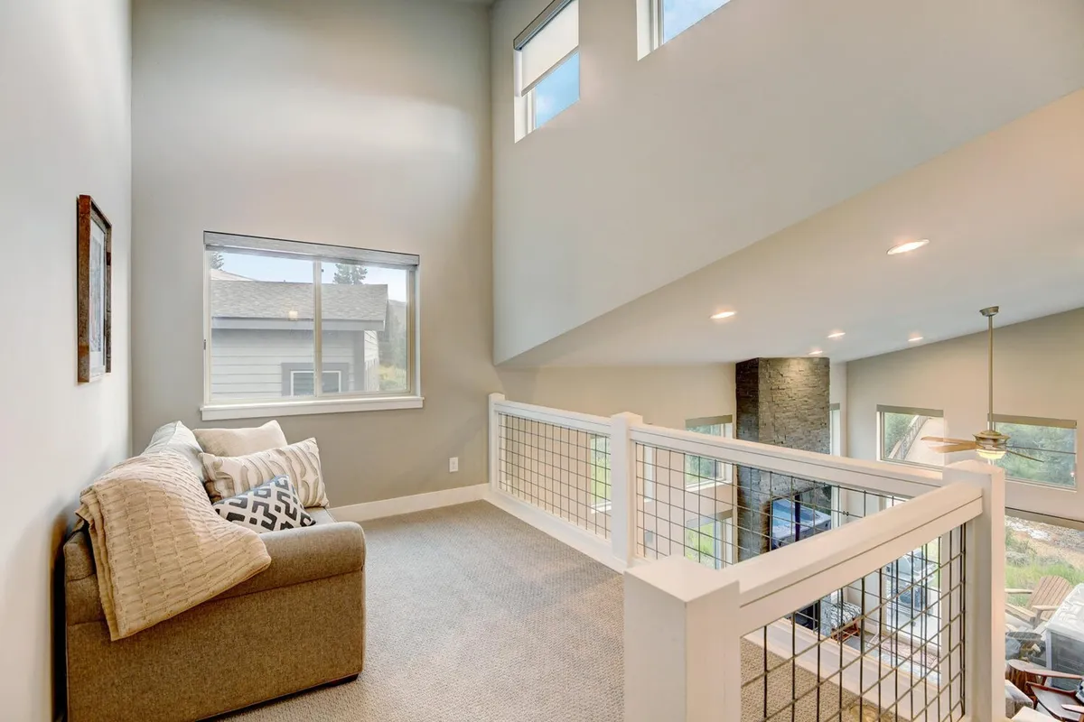 An inviting loft area with a comfortable sofa adorned with decorative pillows, a stylish railing, and expansive windows filling the space with natural light. The ambiance is relaxed and flexible, ideal for additional sleeping or lounging.