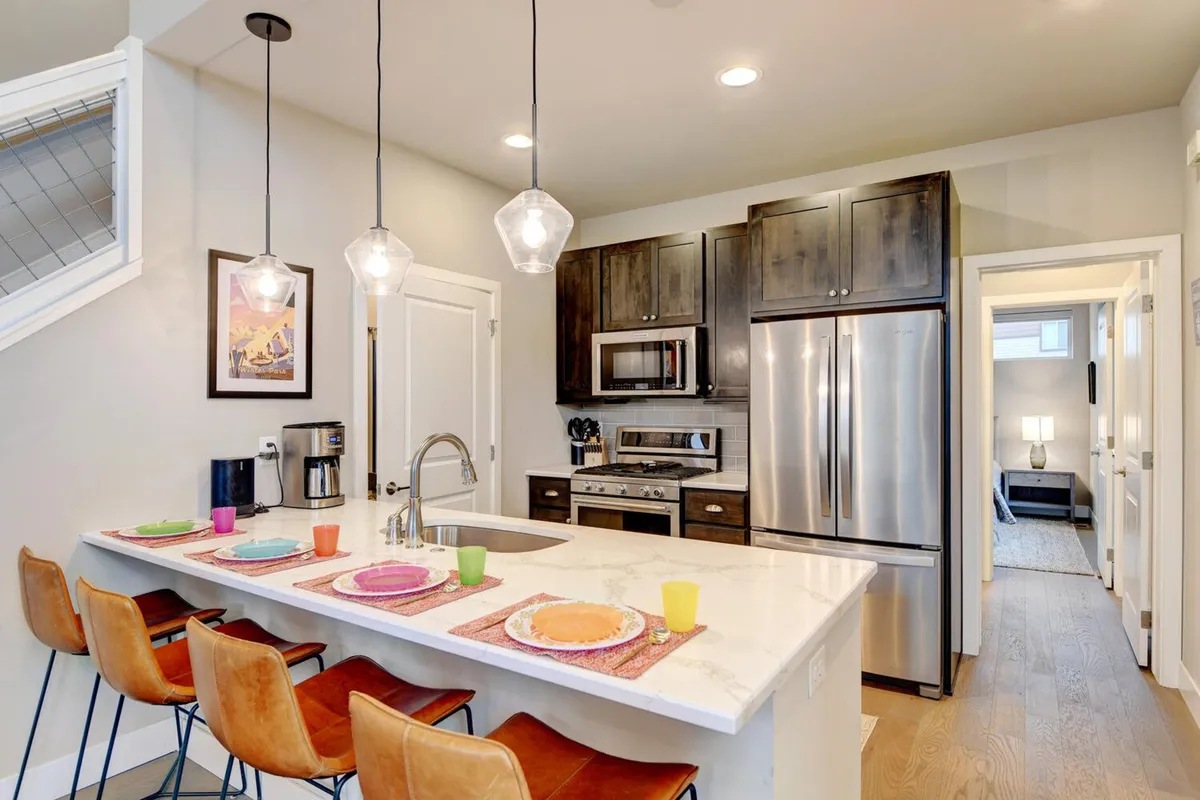 A modern, inviting kitchen interior featuring a central island with colorful plates, high-end appliances, and elegant light fixtures. The scene evokes a sense of warmth and sociability, ideal for family gatherings, entertaining, and preparing special meals together.