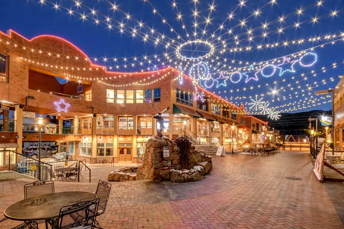 An outdoor plaza adorned with decorative string lights, a stone fountain, and cozy seating areas. The joyful mood is amplified by people dining and socializing, suggesting vibrant community events and upscale experiences within easy reach.
