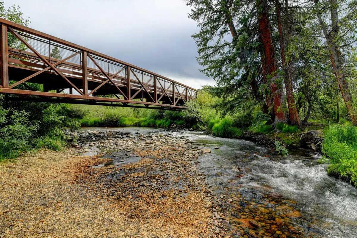 A peaceful scene with a small bridge spanning a gently flowing river surrounded by trees and rocks. The setting captures the tranquility and beauty of the natural environment, making it ideal for outdoor activities in any season.