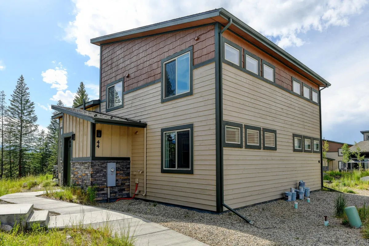 The image shows a modern home exterior with striking stone accents and expansive windows, set against a backdrop of mountain vistas as the sun sets. The inviting architectural style hints at both privacy and sophistication, while the outdoor areas suggest opportunities for relaxation and gathering.