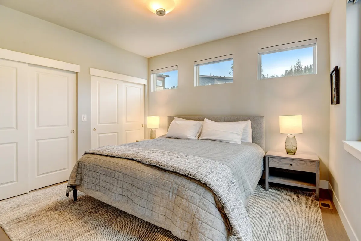 A serene bedroom featuring a cozy bed with plush bedding, a nightstand with a lamp, and large windows that let in natural light. The overall mood is tranquil and restful, inviting occupants to unwind after a long day.