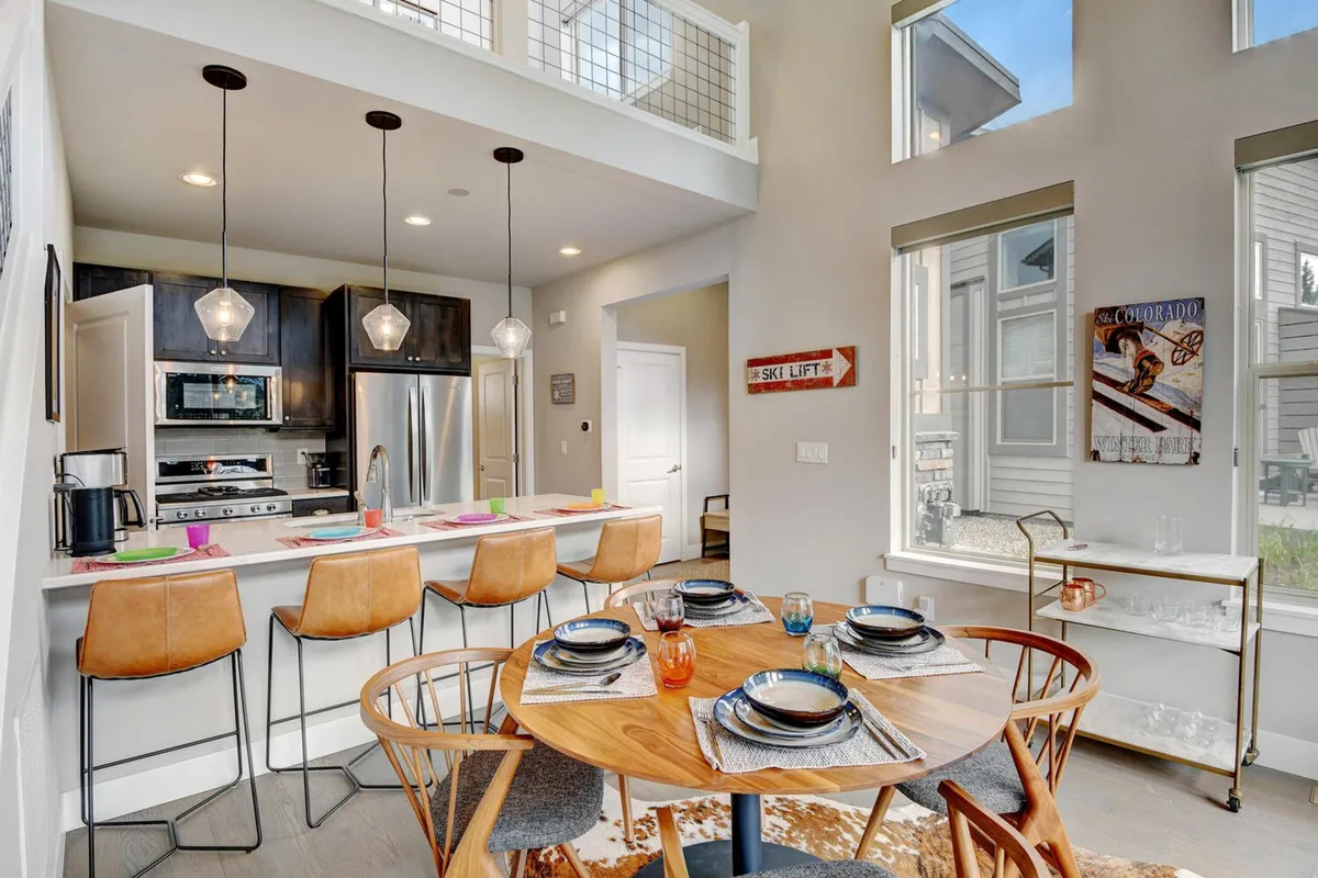 This image captures a modern, open-concept interior featuring a spacious kitchen island, a large dining table, and walls of windows that flood the space with natural light. Sleek appliances and thoughtful lighting contribute to a welcoming, contemporary atmosphere perfect for cooking, dining, and socializing.