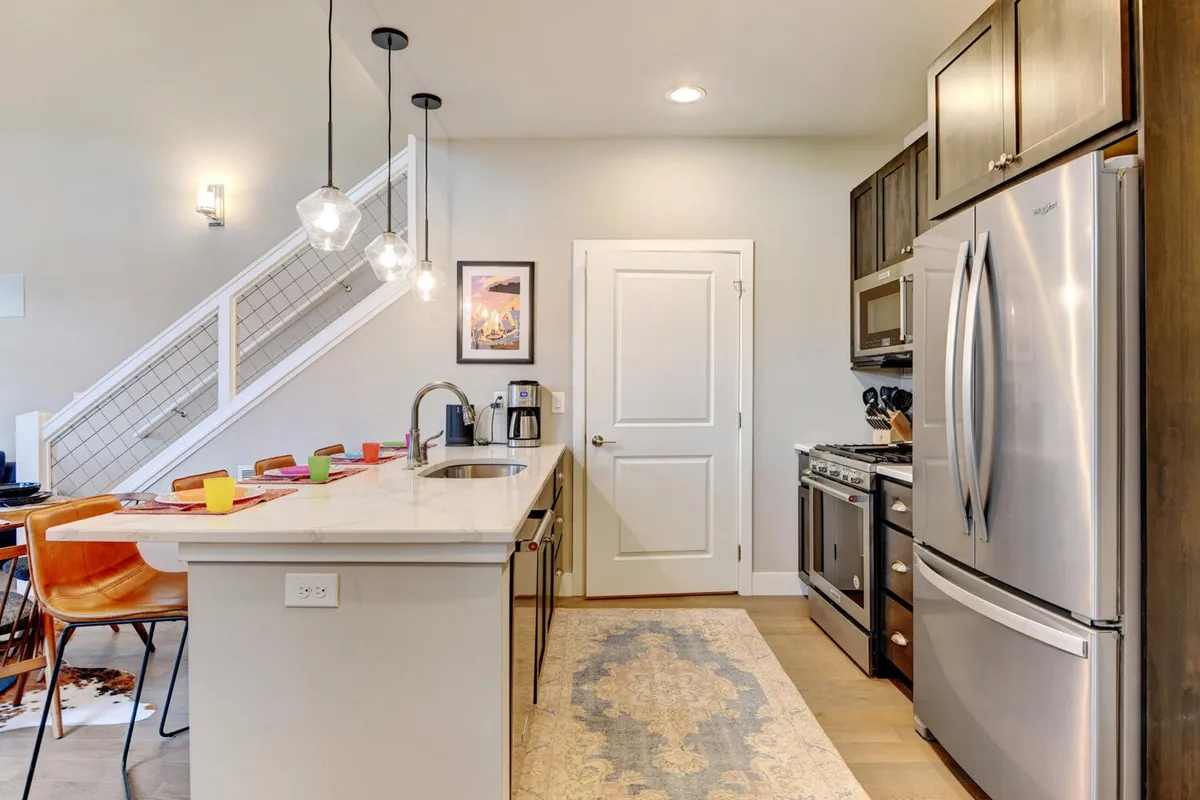 An inviting kitchen scene with a central island, elegant pendant lights, stainless steel appliances, and a decorative rug. The space is set up for both casual breakfasts and festive family dinners, with ample counter space for meal prep and morning coffee.