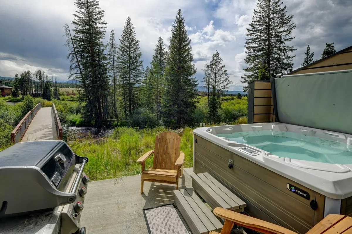 This image features a private hot tub surrounded by adirondack chairs, a grill, and a wooden walkway nestled among the trees. The setup exudes tranquility and encourages relaxation, with views that likely overlook a natural setting.